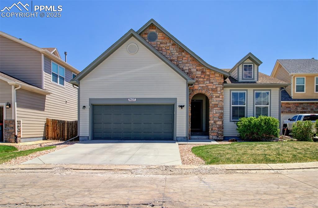 Caption: View of front of property with stone siding, driveway, a front lawn, and an attached garage