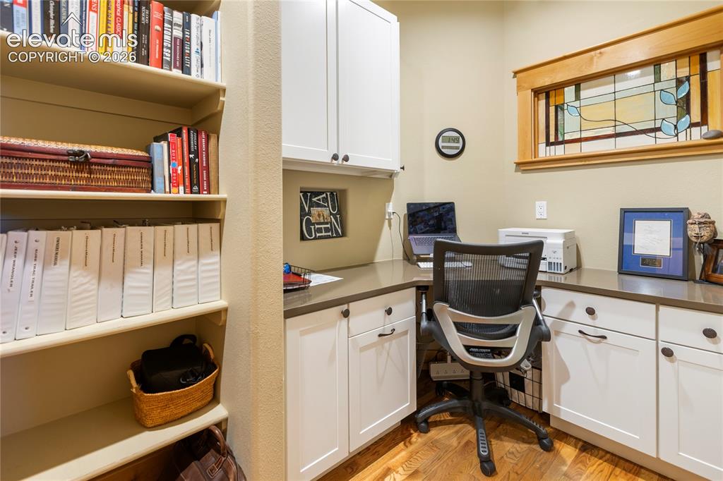 Image 27 of 36: Built-in desk area featuring white cabinetry, dark countertops, and wood-fi