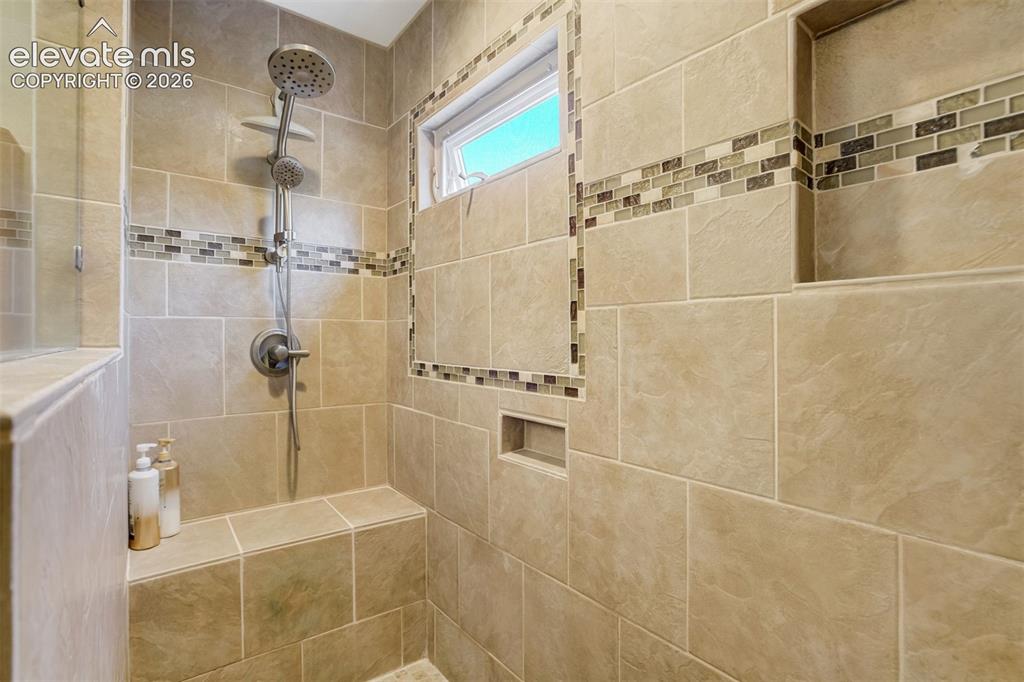Image 25 of 50: Bathroom featuring a walk-in shower with tiled walls and a decorative mosai
