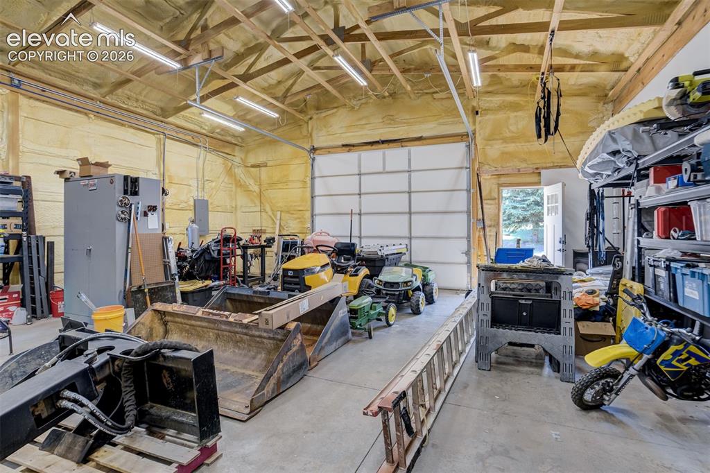 Image 48 of 50: Spacious garage with insulation, fluorescent lighting, a large roll-up door