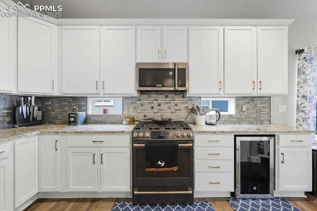 Image 14 of 47: Kitchen with white cabinetry, wine cooler, gas stove, stainless steel micro