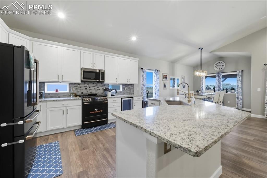 Image 16 of 47: Kitchen featuring backsplash, black appliances, hanging light fixtures, a l