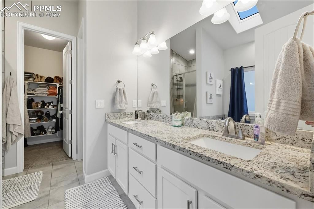 Image 23 of 47: Bathroom featuring a stall shower, a walk in closet, double vanity, a skyli