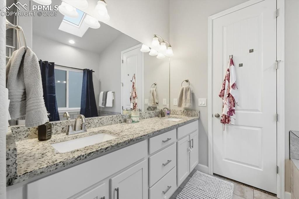 Image 24 of 47: Bathroom featuring a skylight, double vanity, and light tile patterned floo