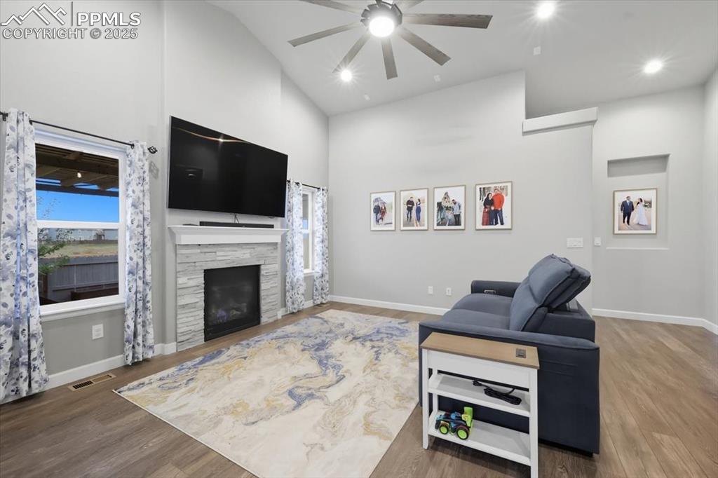 Image 8 of 47: Living area featuring high vaulted ceiling, wood finished floors, a stone f