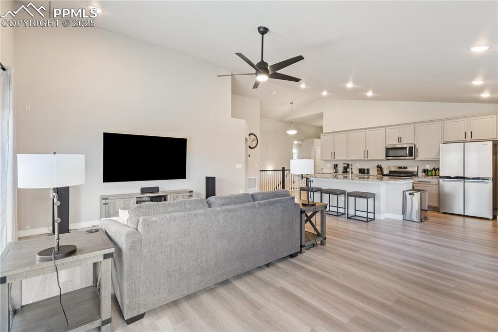 Image 15 of 46: Living room with light wood-type flooring, a ceiling fan, high vaulted ceil