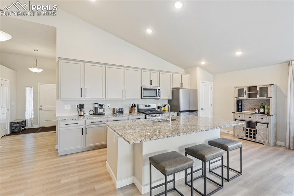 Image 18 of 46: Kitchen with light wood-style flooring, a breakfast bar, light stone counte
