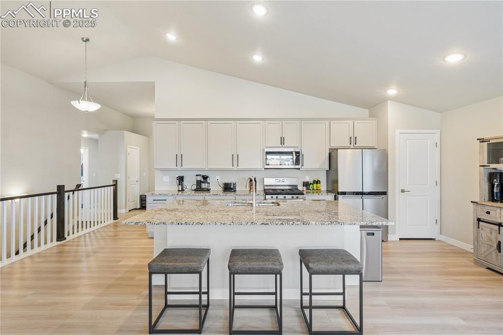Image 8 of 46: Kitchen featuring a breakfast bar area, light stone counters, appliances wi