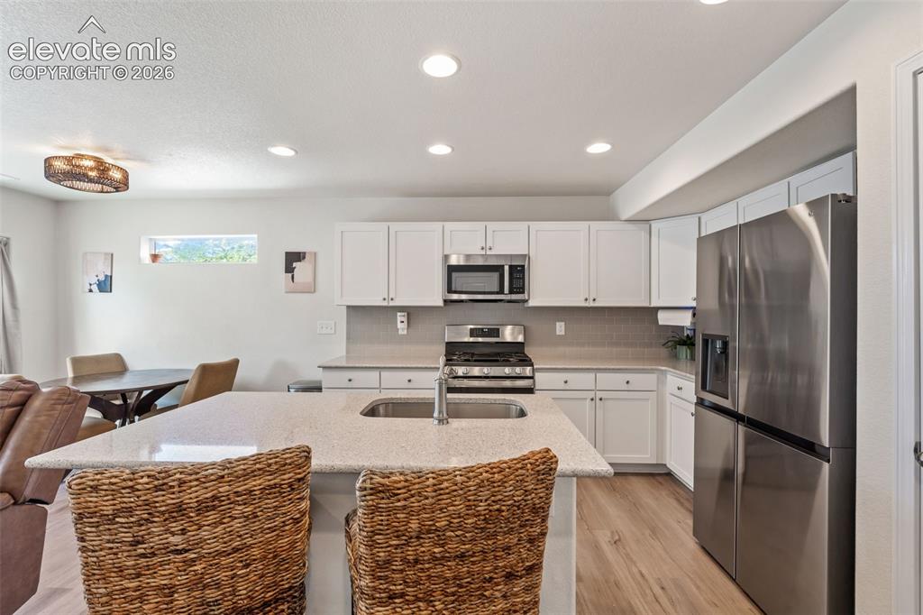 Image 13 of 38: Open-concept kitchen featuring white cabinetry, stainless steel appliances,
