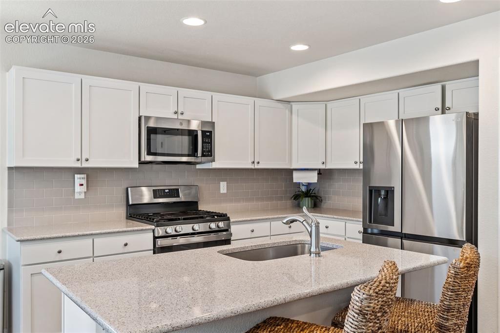 Image 14 of 38: Modern kitchen featuring stainless steel appliances, white cabinetry, a neu