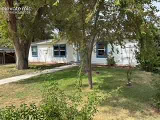 Caption: White siding exterior featuring blue window trim, a concrete walkway, and established trees