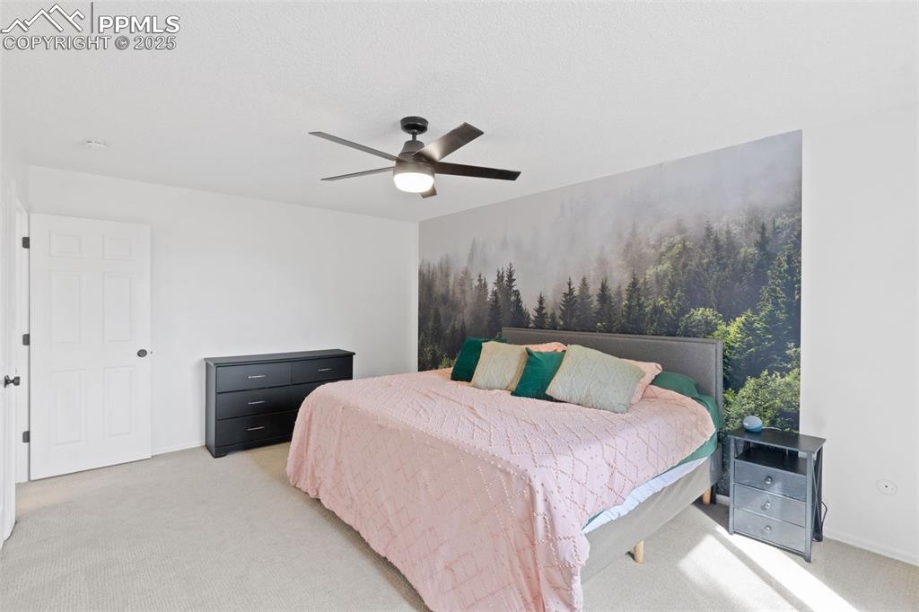 Image 10 of 24: Large primary bedroom upstairs with light carpet and a ceiling fan. Wall pa