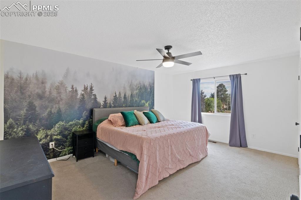 Image 11 of 24: Large primary bedroom with light carpet, a ceiling fan, a textured ceiling,