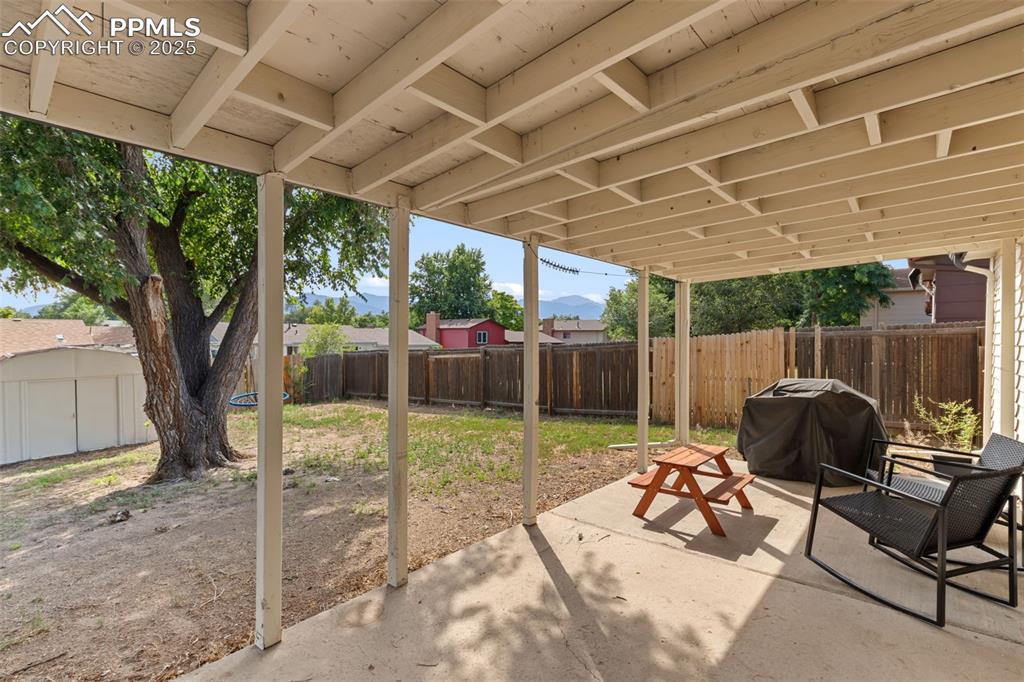 Image 20 of 24: Fenced backyard featuring a covered patio area, large shade tree and mounta