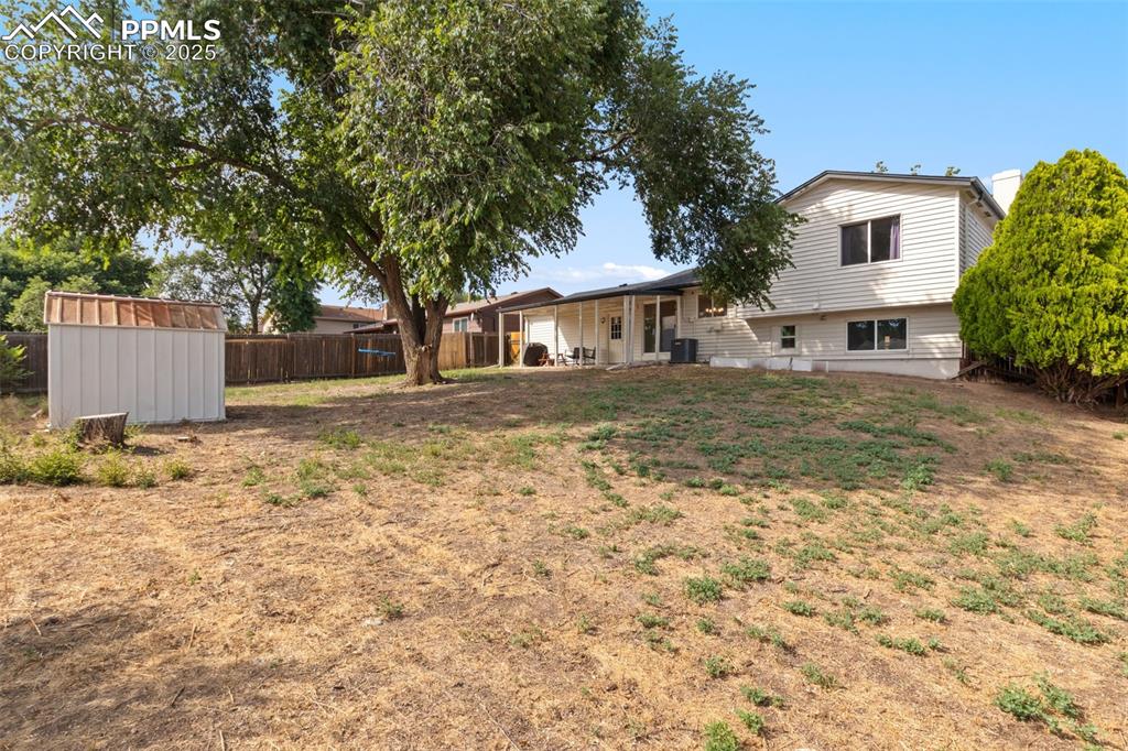 Image 23 of 24: Large backyard with storage shed, covered patio and large shade tree.
