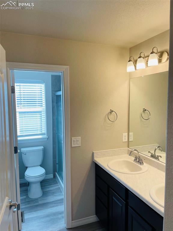 Image 10 of 19: Bathroom featuring double vanity, light wood-type flooring, and a stall sho
