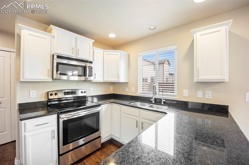 Image 10 of 39: Kitchen with stainless steel appliances, dark stone counters, white cabinet