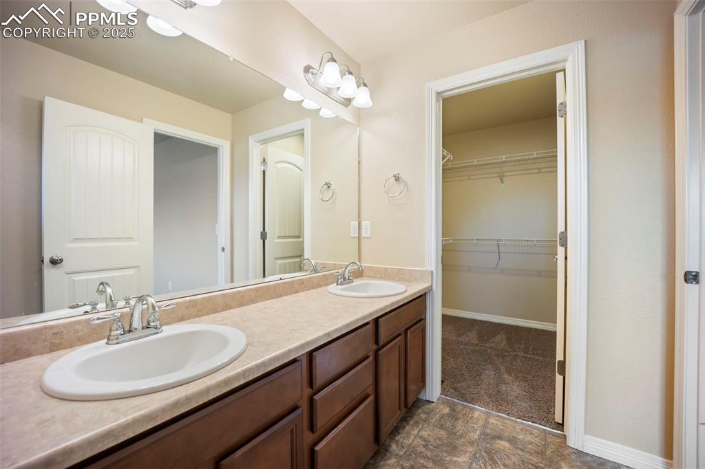 Image 24 of 39: Bathroom with double vanity, a walk in closet, and stone finish floors
