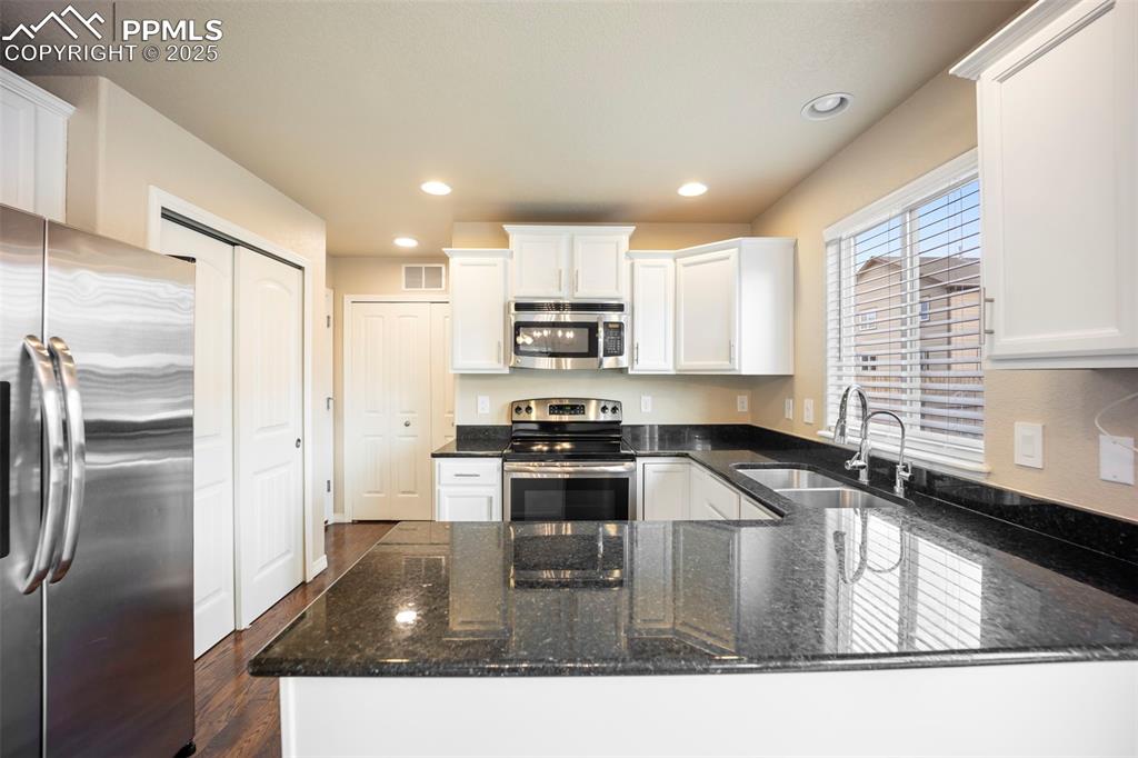 Image 8 of 39: Kitchen featuring stainless steel appliances, dark stone countertops, white