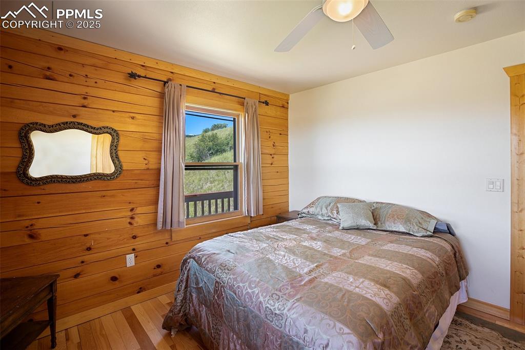 Image 13 of 28: Bedroom with wood finished floors, wooden walls, and a ceiling fan
