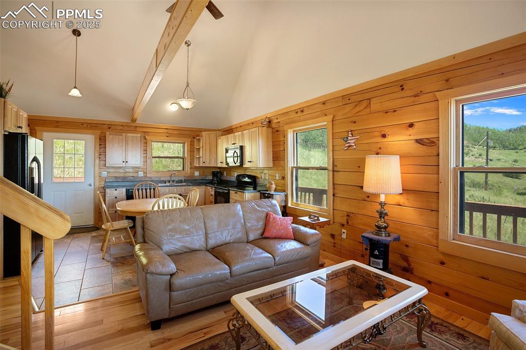 Image 7 of 28: Living room featuring high vaulted ceiling, beamed ceiling, wood walls, and