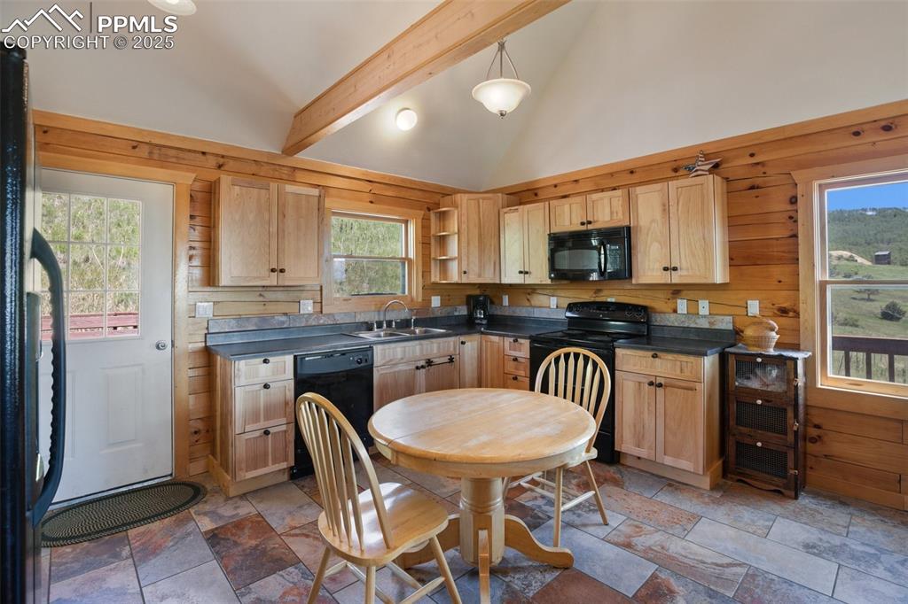 Image 8 of 28: Kitchen with black appliances, dark countertops, open shelves, stone tile f