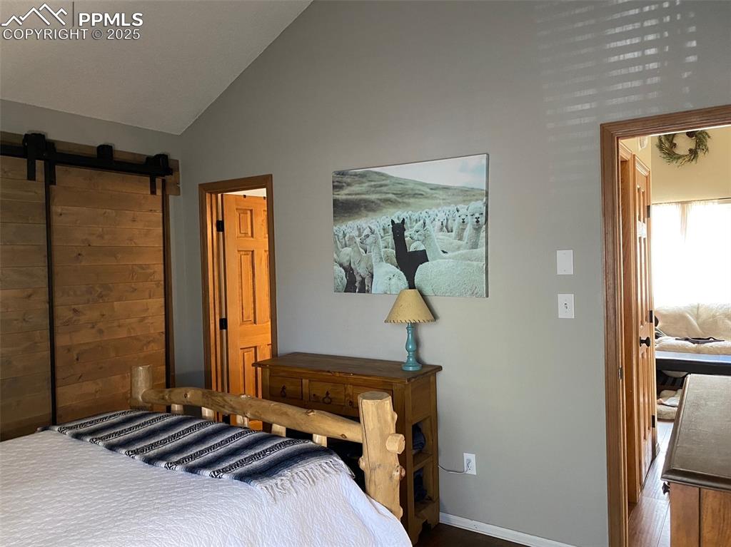 Image 9 of 16: Bedroom with a barn door, vaulted ceiling, and wood finished floors