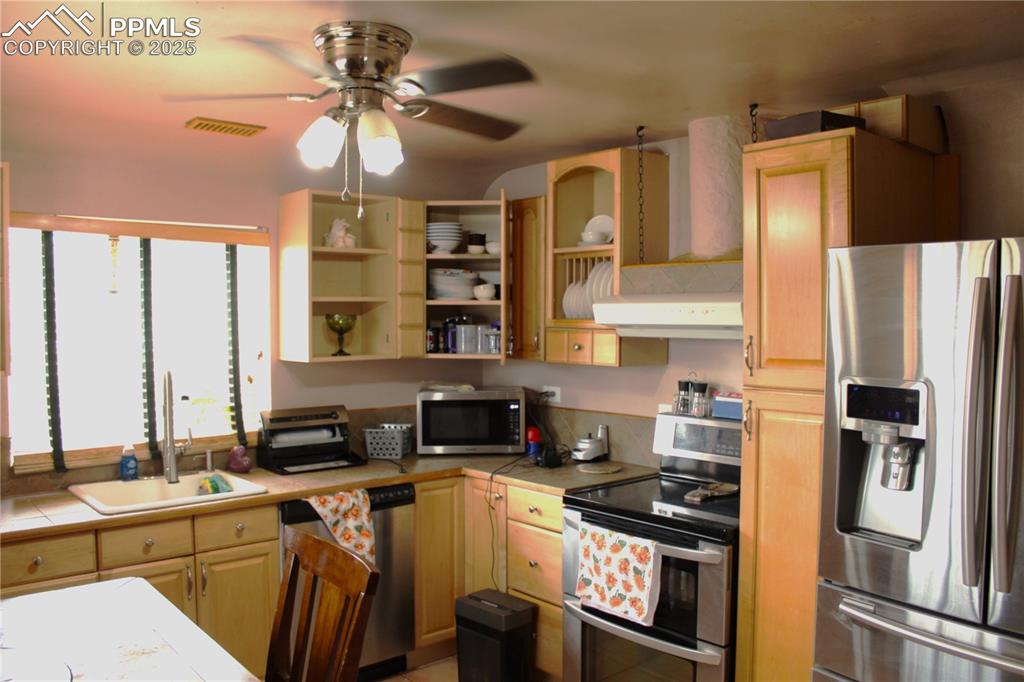 Image 15 of 41: Kitchen with stainless steel appliances, tile countertops, open shelves, ce