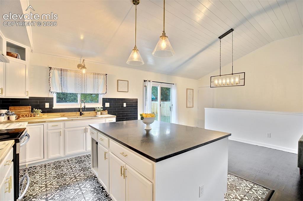 Image 15 of 43: Kitchen featuring a central island with a dark countertop, white cabinetry
