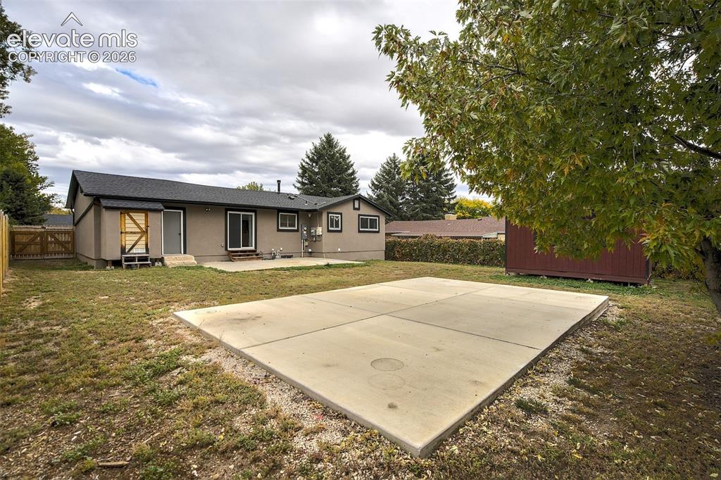Image 42 of 43: Rear exterior featuring a concrete patio, detached storage structure, and f
