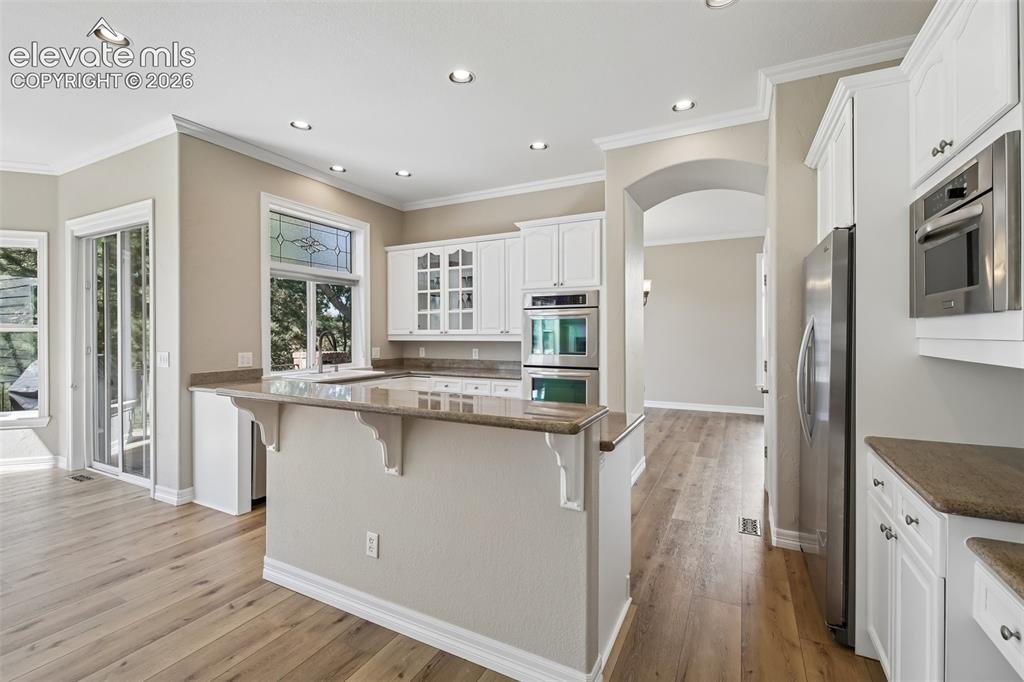 Image 12 of 49: Kitchen featuring white cabinetry, light-toned countertops, wood-finish flo