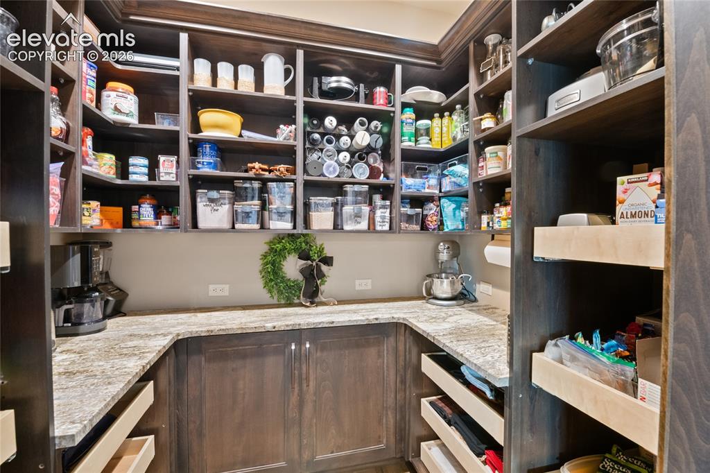 Image 14 of 50: Expansive walk-in pantry featuring granite counters, custom shelving, pull-