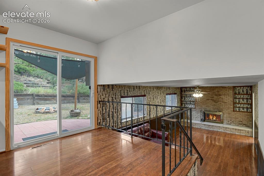 Image 11 of 35: Wood-finish flooring, sliding glass door, metal railing, brick fireplace su