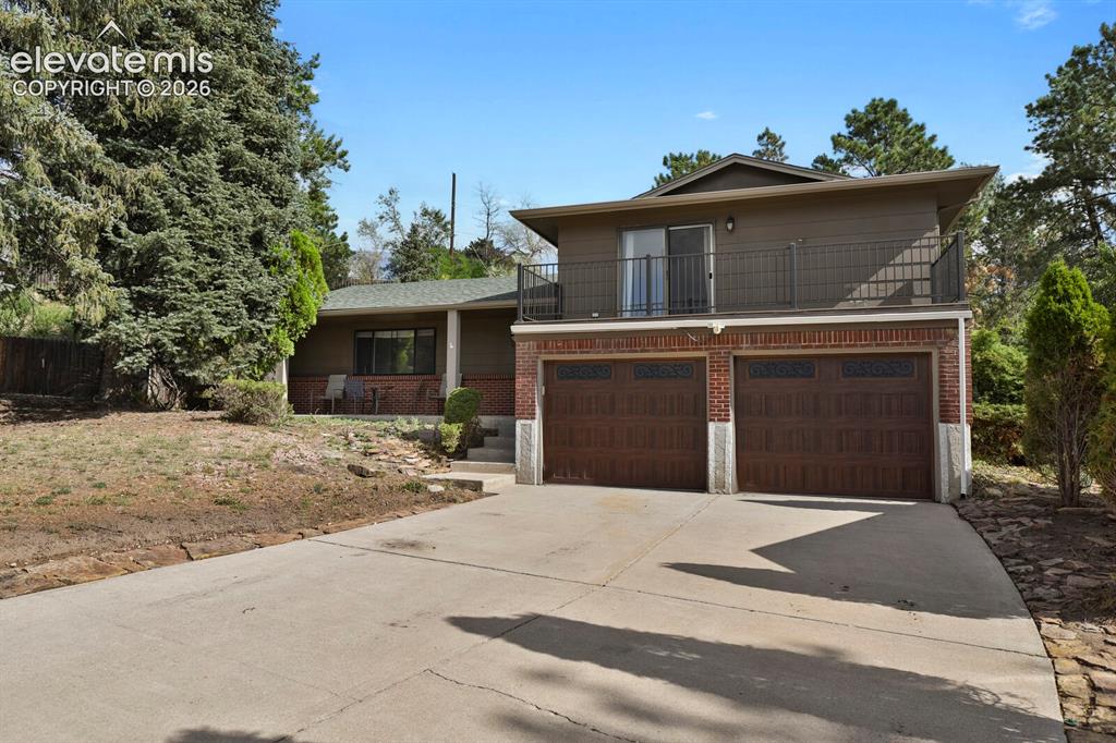 Image 3 of 35: Two-car garage with wood-finish doors, brick facade, and an upper-level bal