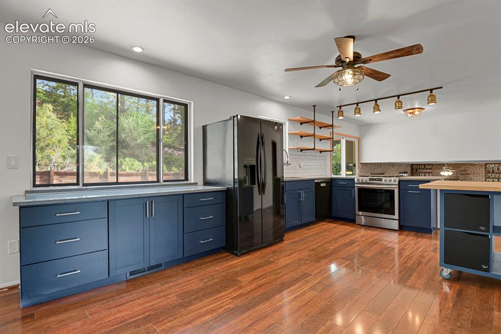 Image 9 of 35: Wood-finish flooring with navy cabinetry, stainless steel appliances, and a