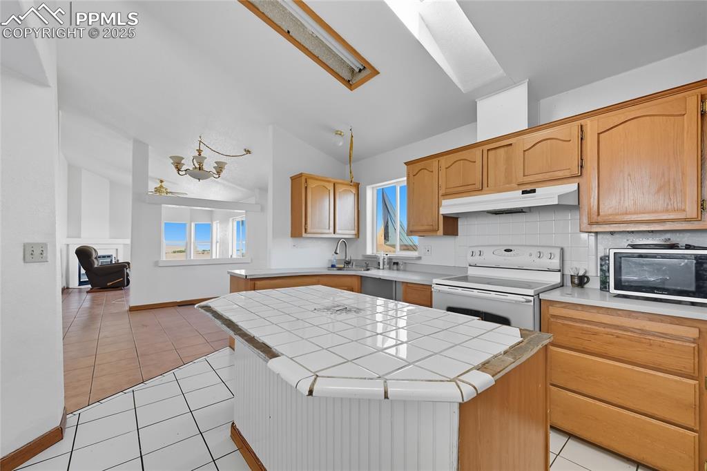 Image 13 of 28: Kitchen with tile counters, light tile patterned floors, tasteful backsplas