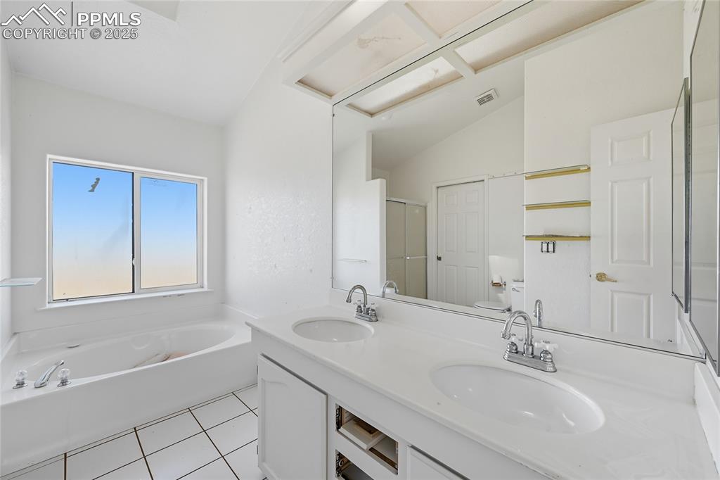 Image 7 of 28: Bathroom with light tile patterned floors, a garden tub, double vanity, lof