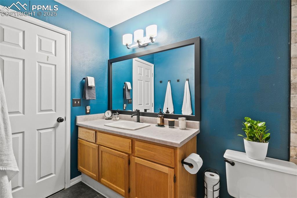 Image 12 of 27: Half bathroom with vanity, a textured wall, and dark tile patterned floors
