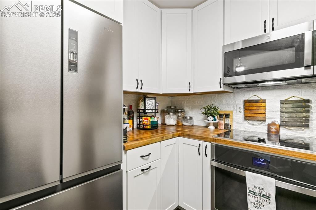 Image 16 of 27: Kitchen with stainless steel appliances, white cabinetry, tasteful backspla