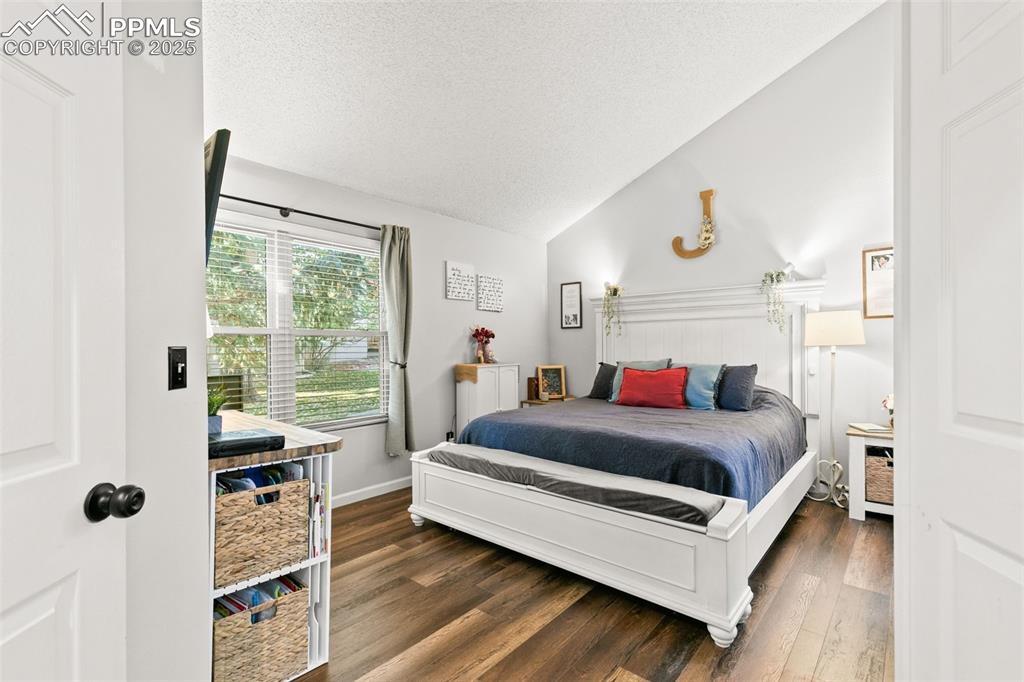 Image 7 of 27: Bedroom featuring lofted ceiling, a textured ceiling, and dark wood finishe