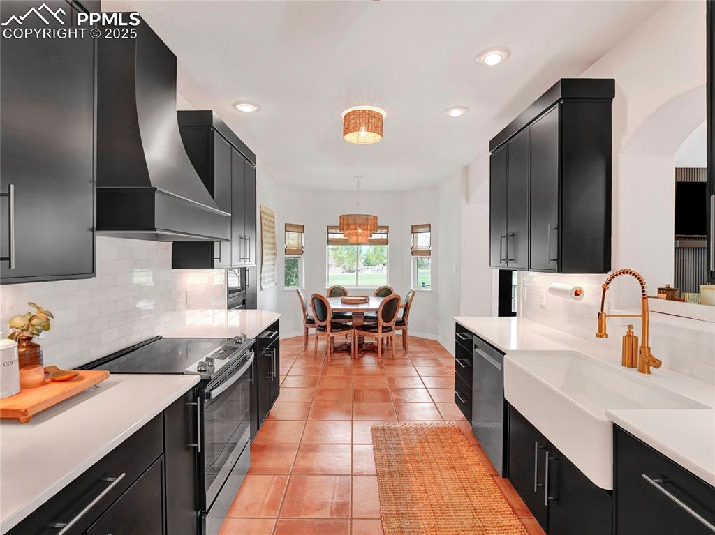 Image 11 of 44: Kitchen with dark cabinetry, stainless steel appliances, wall chimney exhau