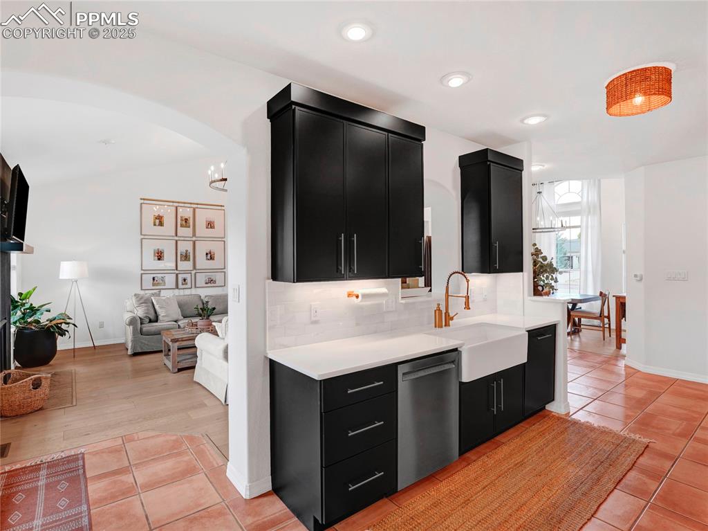 Image 13 of 44: Kitchen featuring dark cabinetry, stainless steel dishwasher, a sink, light