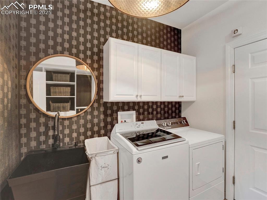 Image 21 of 44: Laundry room with cabinet space, washer and clothes dryer, and wallpapered