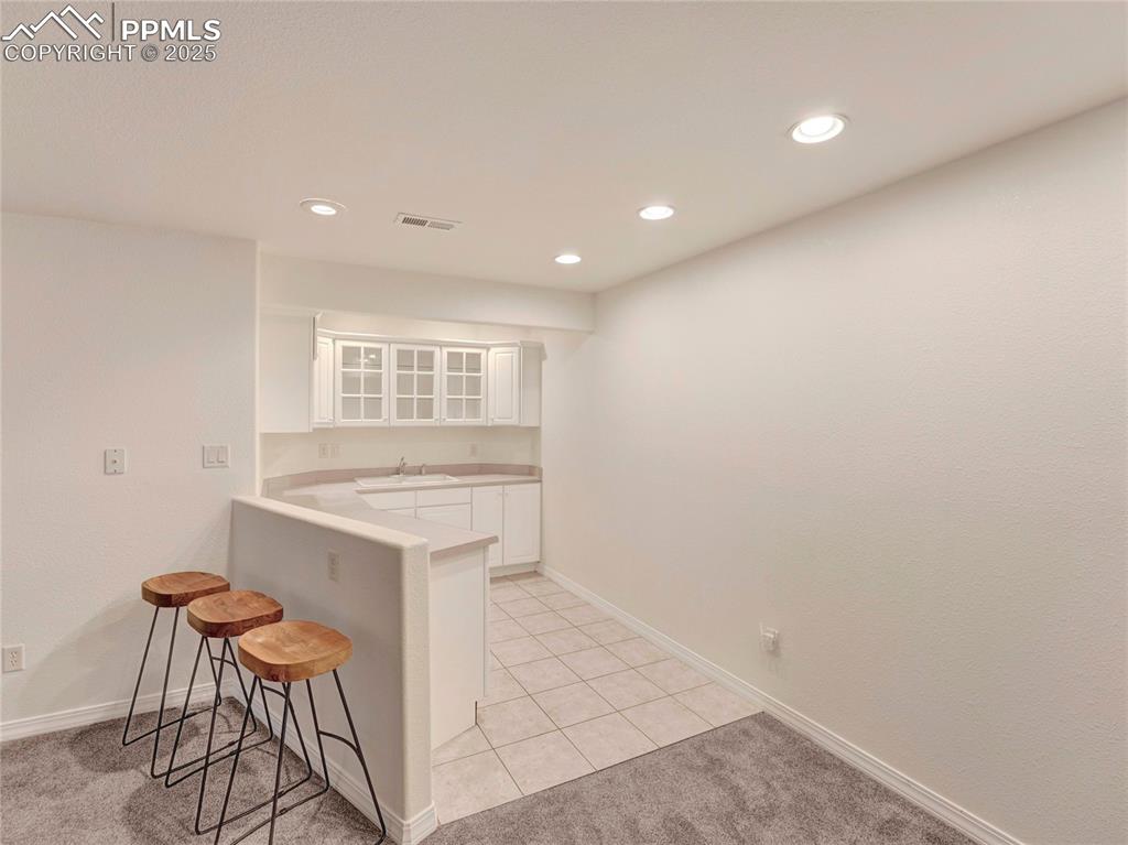 Image 31 of 44: Kitchen featuring a kitchen bar, white cabinetry, a peninsula, a sink, and