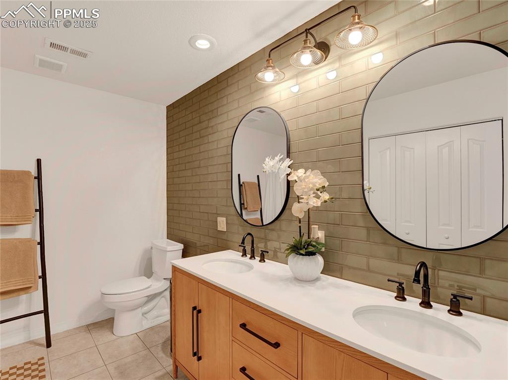 Image 36 of 44: Full bath with tile walls, tile patterned flooring, toilet, double vanity,