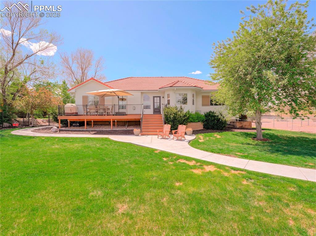 Image 40 of 44: Rear view of property with a wooden deck, a tile roof, a lawn, and stucco s