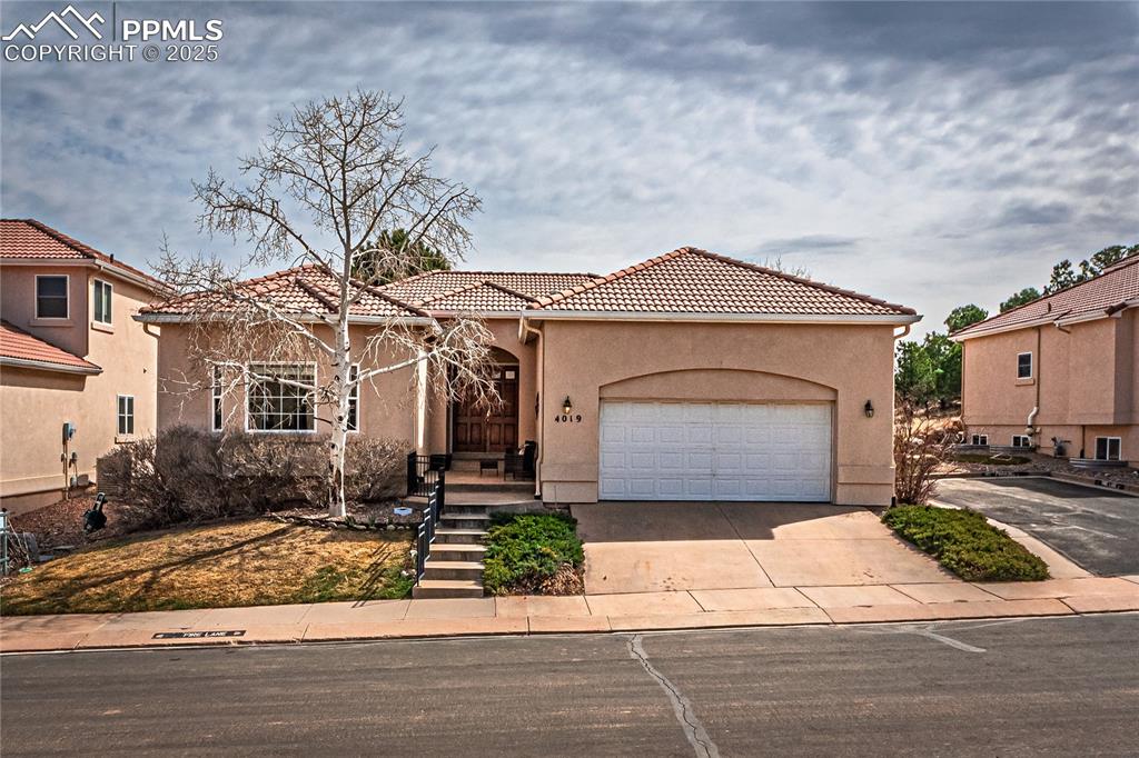 Caption: Mediterranean / spanish home featuring driveway, a garage, a tiled roof, and stucco siding