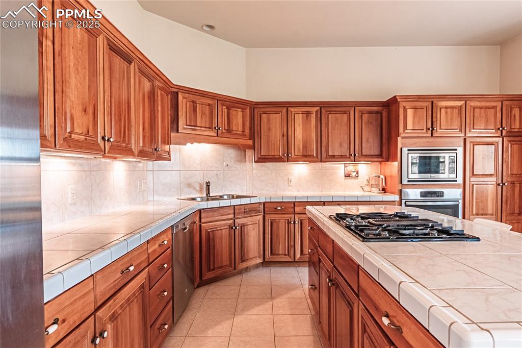 Image 14 of 49: Kitchen with brown cabinets, a sink, appliances with stainless steel finish
