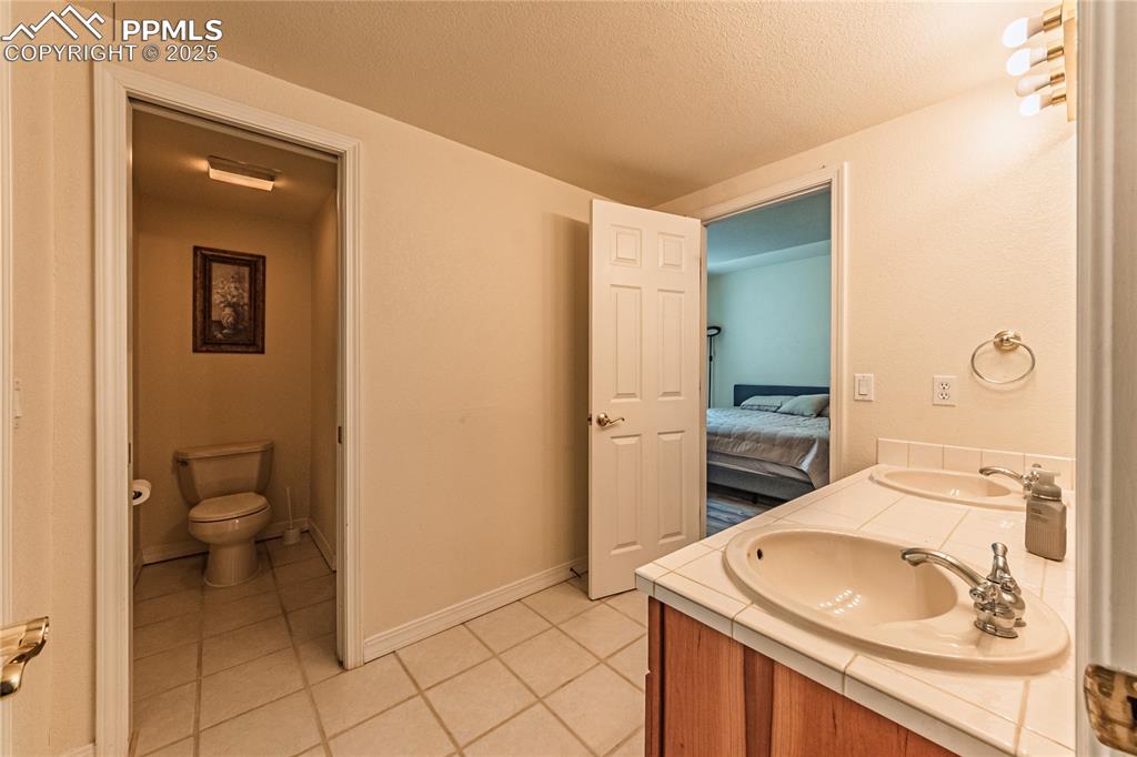 Image 28 of 49: Ensuite bathroom with a textured ceiling, toilet, a sink, tile patterned fl