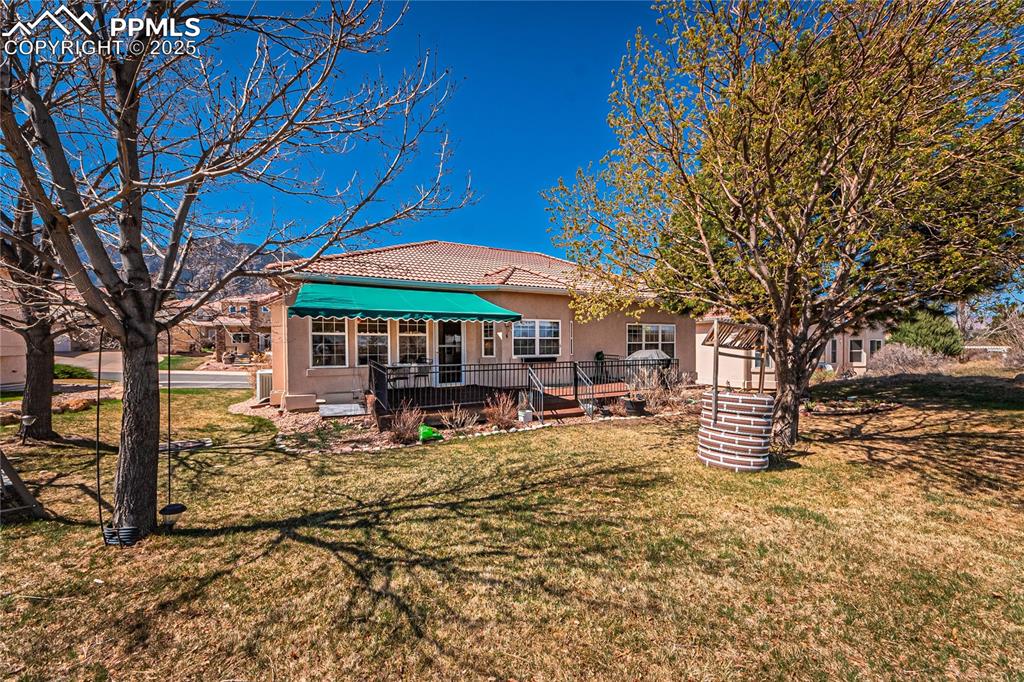 Image 41 of 49: Back of house featuring a tile roof, a deck, a lawn, and stucco siding